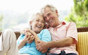 An elderly couple with implant supported dentures smiling and embracing.