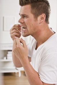 A man flossing his teeth, preventing infection that leads to root canals in Roy.