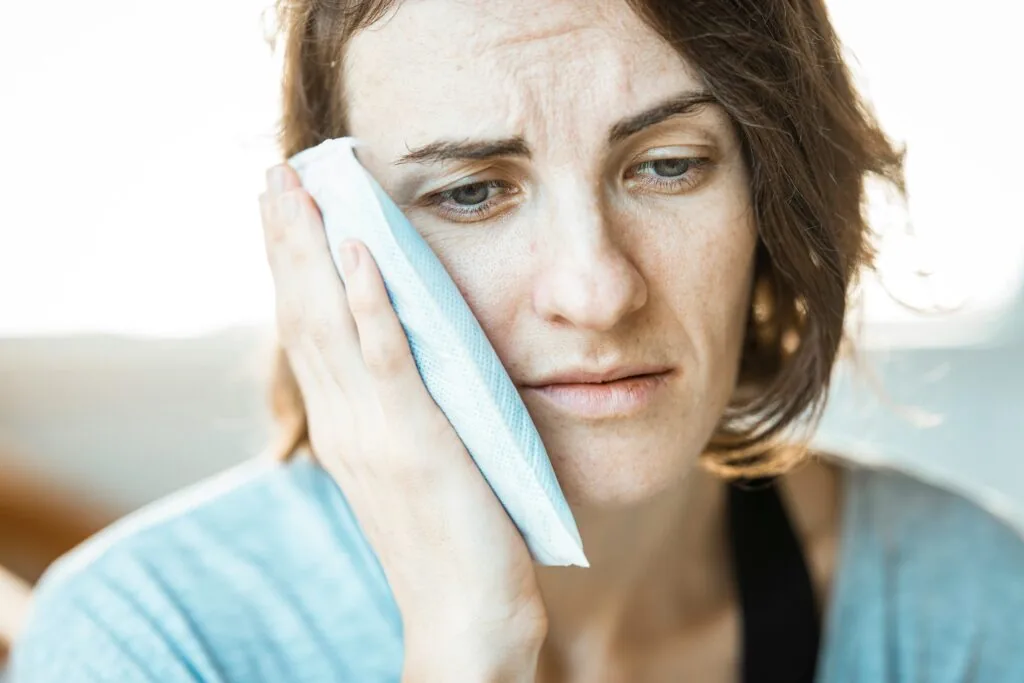 Woman holds a compress up to her face because of emergency tooth pain.